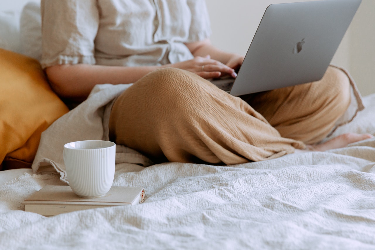 person in bed with laptop and coffee