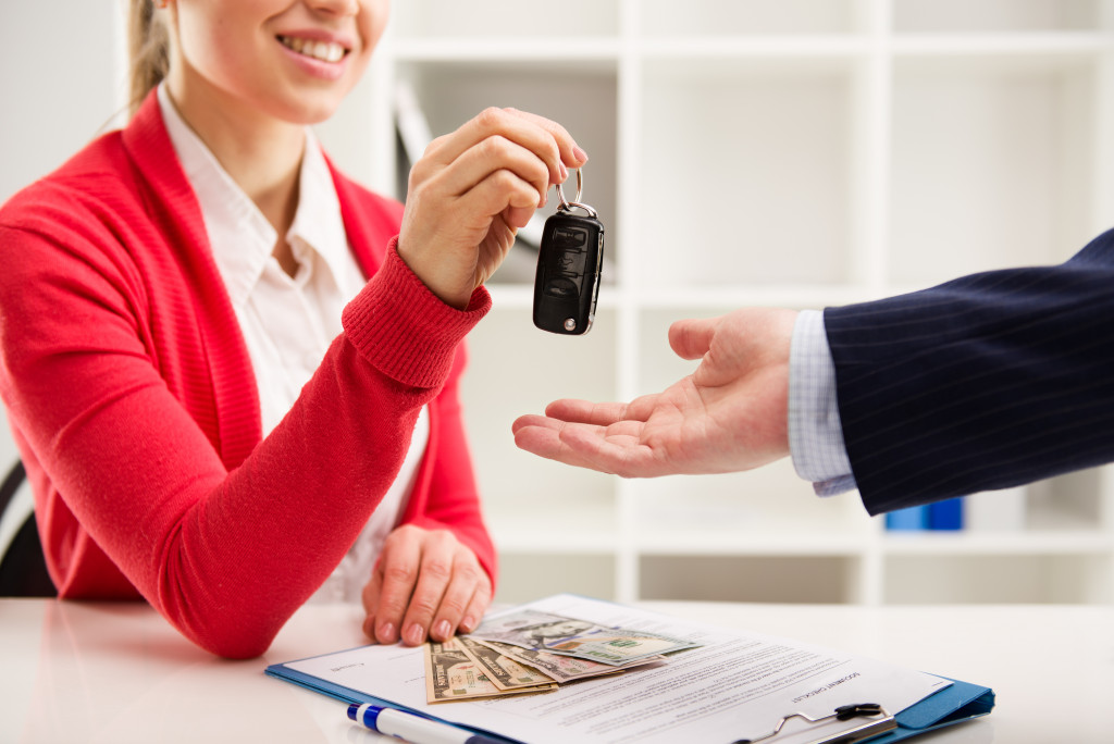 Rental contract. Transport purchase. Woman automotive dealer offering car key to buyer. Shallow depth of field.