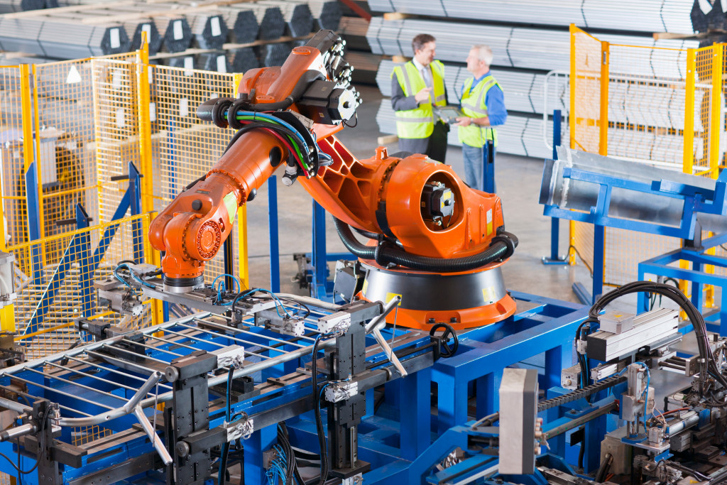 Wide angle shot of Business Man and Worker controlling robotic machinery lifting steel fencing in manufacturing plant