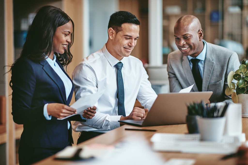 Smiling group of diverse businesspeople going over paperwork together and working on a laptop at a table in an office