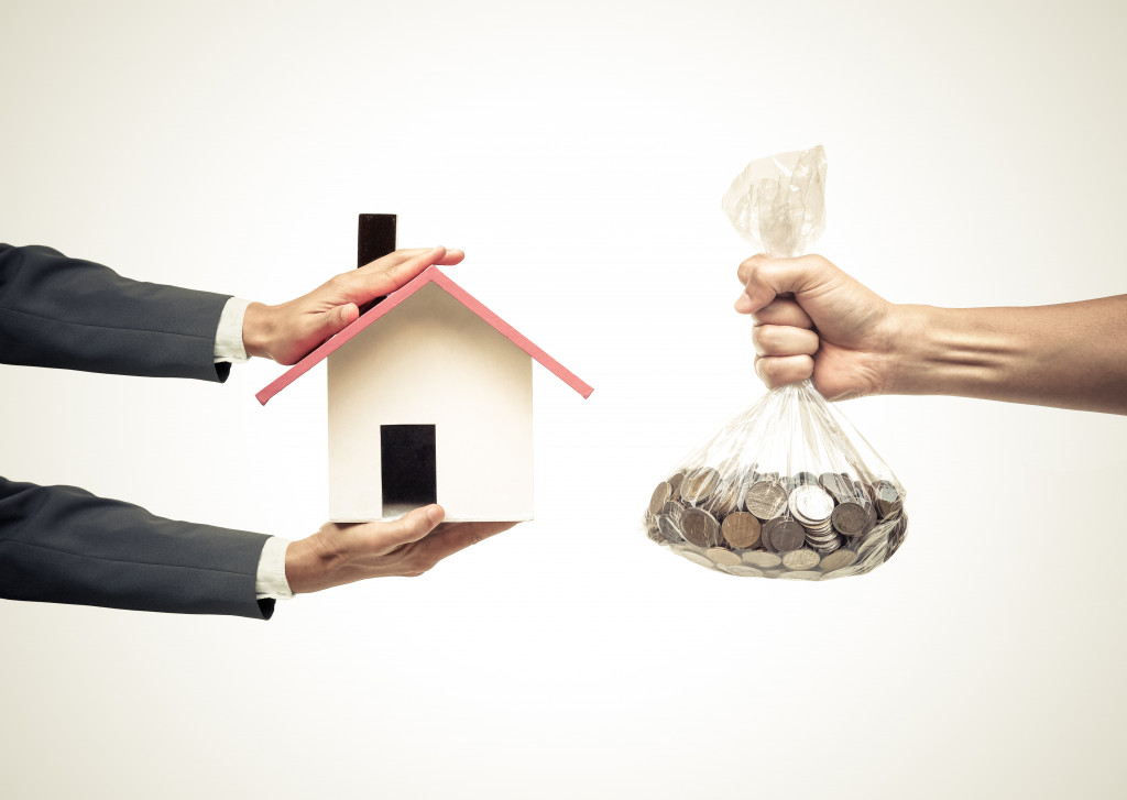 Hands exchanging toy house and bag of coins