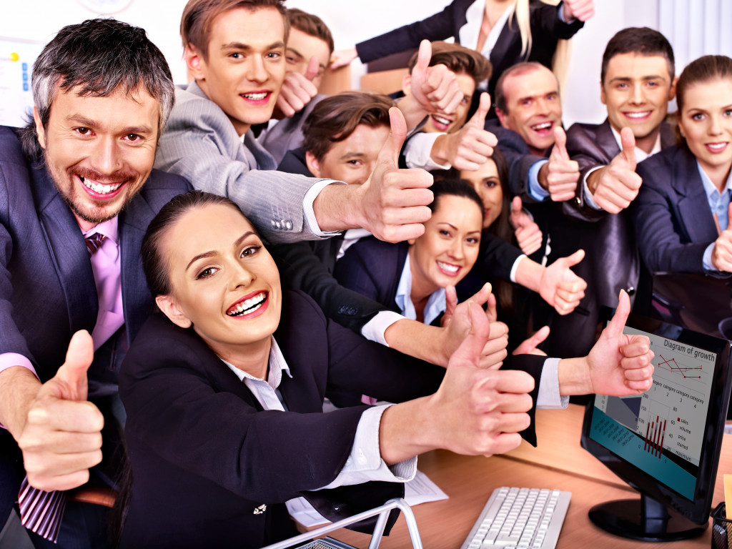 Business executives showing a thumbs up sign inside an office.