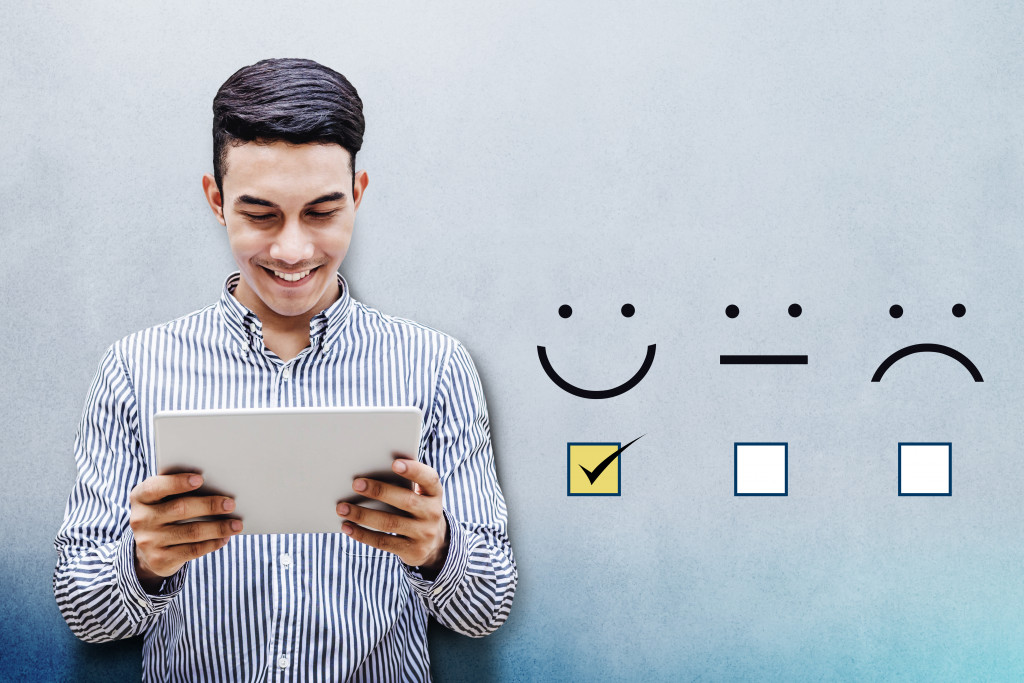 A man holding a tablet with a satisfied rating on a wall beside him