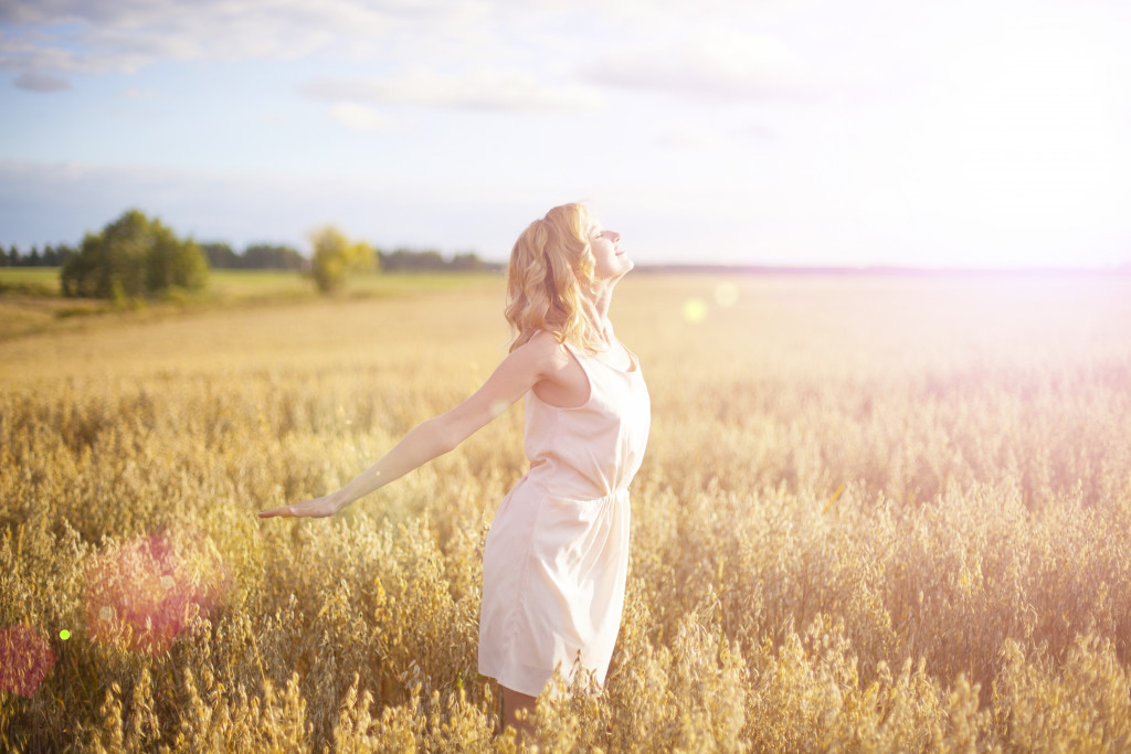 Young woman facing the sun while wearing lightweight clothing in a field.