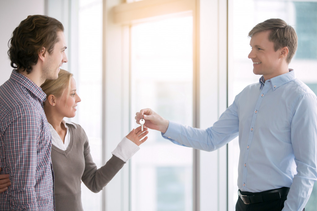 male landlord smiling at young couple tenant being handed the house key