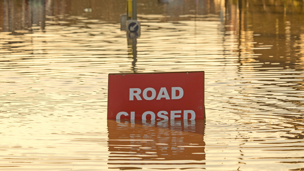 Road closed sign partially covered in a flooded street.