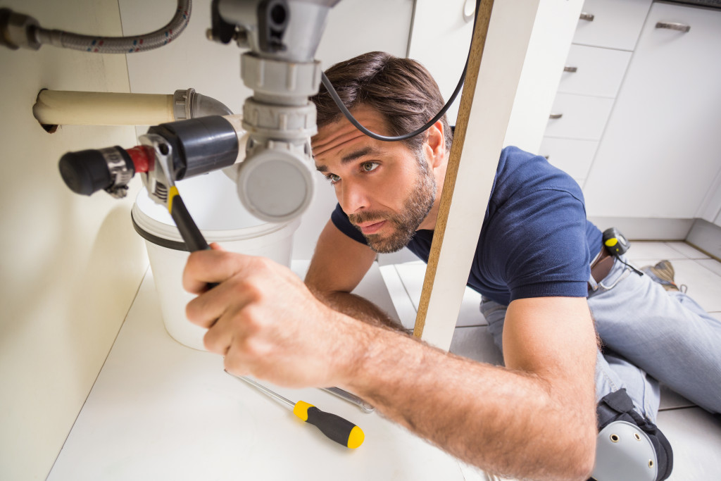 male plumber using tool under the sink in the kitchen