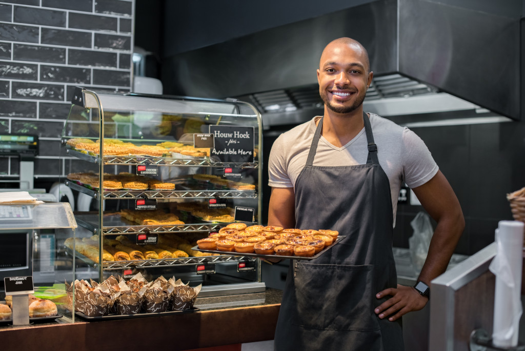 Male business owner holding a tray of pastries in a cafeteria.